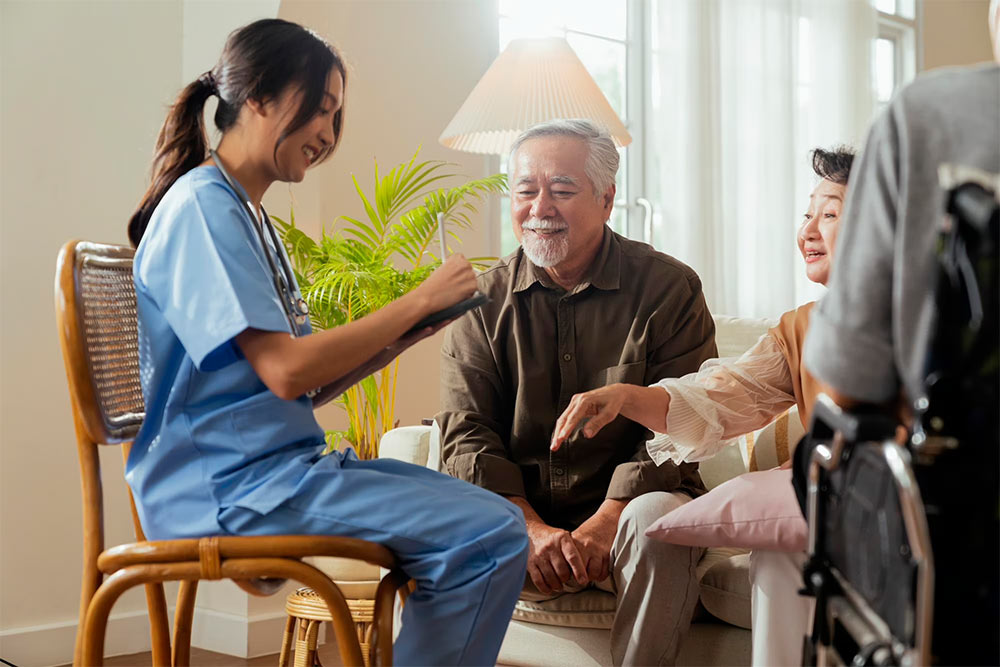 A nurse practitioner smiling with an elderly couple during a home visit